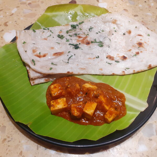 Paneer butter masala served with butter naan on a banana leaf